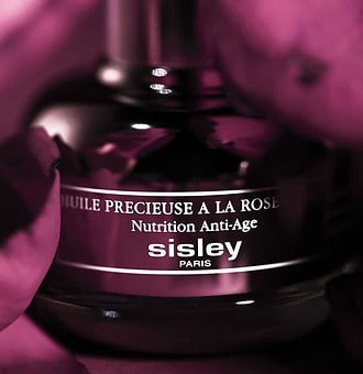 Lotion anti-âge Sisley Paris dans un flacon élégant, entouré de fleurs roses.