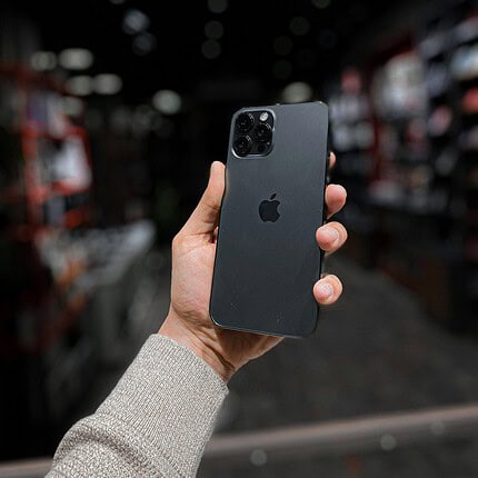 IPhone 13 Pro noir en main, détails des caméras visibles, fonds flou d'un magasin d'électronique.